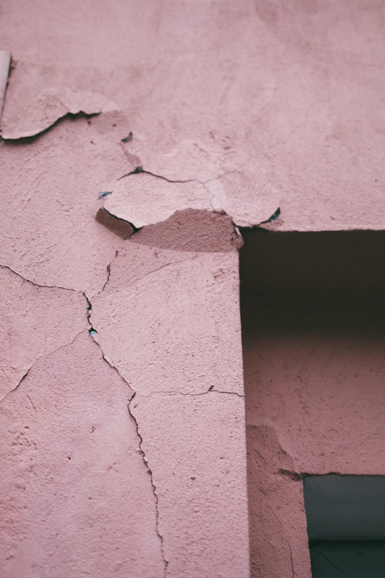 Detailed view of a cracked and weathered pink concrete wall with peeling paint. Systemwandel erst unter Druck