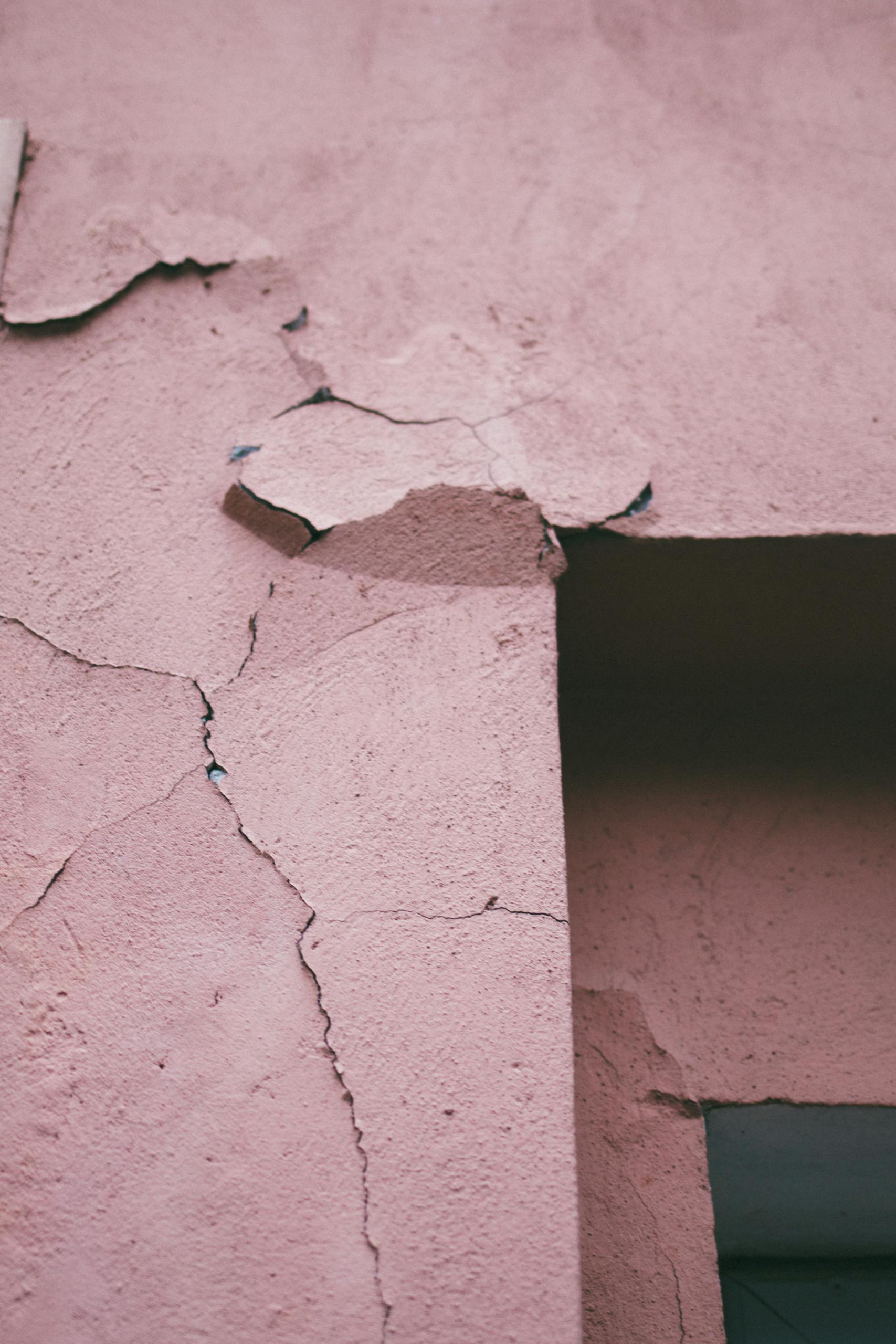 Detailed view of a cracked and weathered pink concrete wall with peeling paint. Systemwandel erst unter Druck