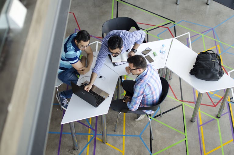 Three men collaborating over a laptop in a modern, geometric-themed office space. Teamwork
