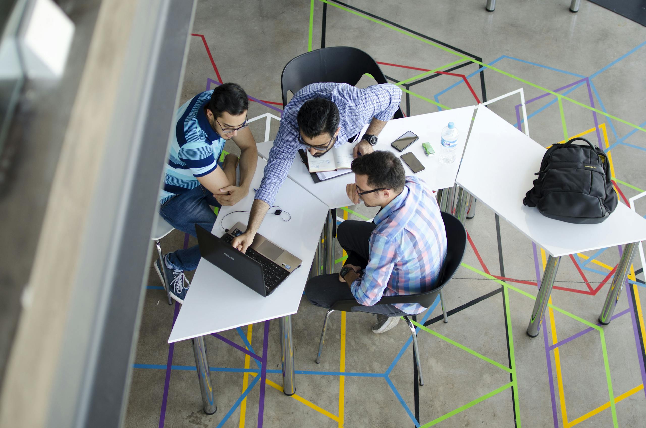 Three men collaborating over a laptop in a modern, geometric-themed office space. Teamwork